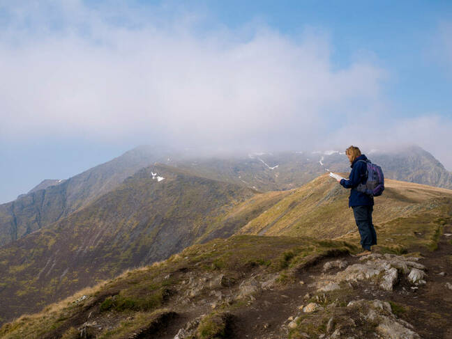 A lone walker looks at a map on the way to the misty summit of Blencathra (also known as Saddleback) in the Lake District, Cumbria, UK with cloud falling against a blue sky A lone walker looks at a map on the way to the misty summit of Blencathra (also known as Saddleback) in the Lake District, Cumbria, UK with cloud falling against a blue sky